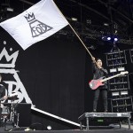 Guitarist Pete Wentz waves a Fall Out Boy flag over the crowd as lead singer Patrick Stump takes a vocal solo. (Credit to Billboards Music.)