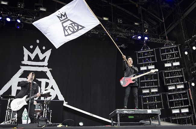 Guitarist Pete Wentz waves a Fall Out Boy flag over the crowd as lead singer Patrick Stump takes a vocal solo. (Credit to Billboards Music.)