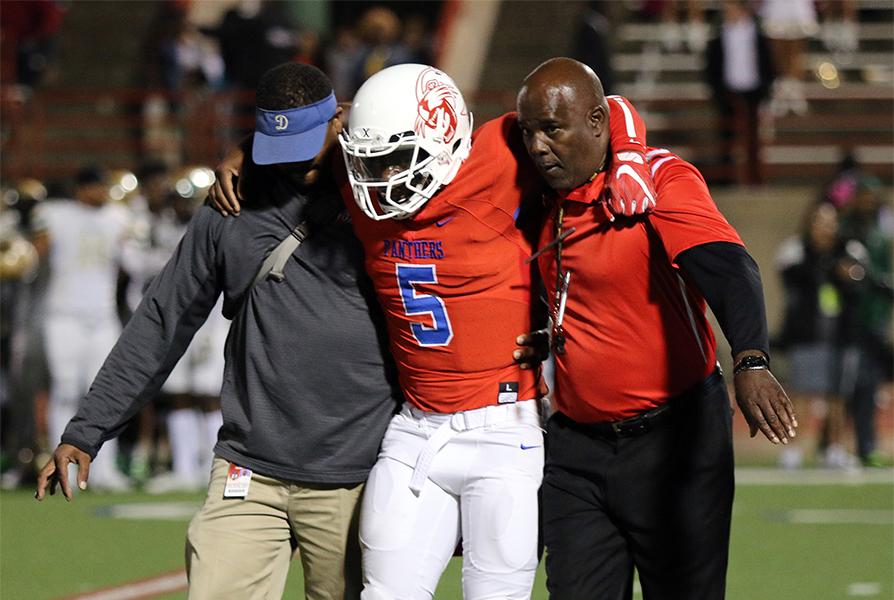 Panther Head Coach Reginald Samples assist trainer Alec Hawkins with giving starting quarterback Jaylin Nelson some support off the field after his season ending injury. (Jose Sanchez photo)